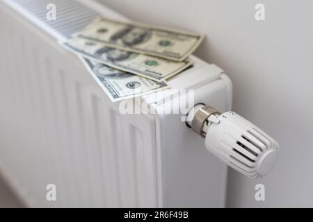 Pile de billets de banque en dollars sur la batterie du radiateur de chauffage avec thermostat. Concept de coûts de chauffage coûteux et de facture énergétique croissante Banque D'Images