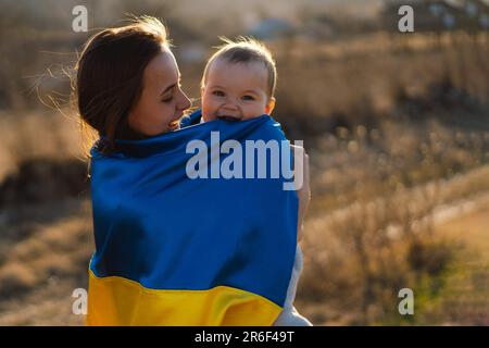 Une femme embrasse son petit fils enveloppé dans le drapeau jaune et bleu de l'Ukraine à l'extérieur. Banque D'Images