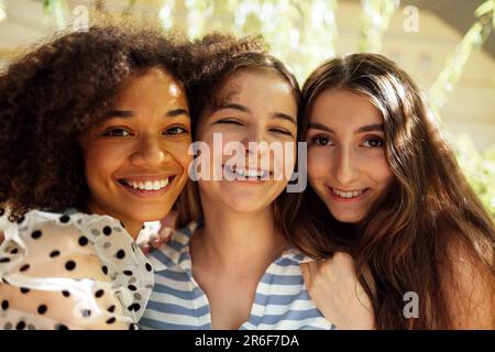 Gros plan portrait de trois jolies adolescentes de différentes nationalités dans des vêtements décontractés posent à l'appareil photo et embrasse. Souriant drôles filles h Banque D'Images