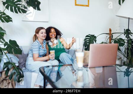 Deux jeunes adorables de différentes nationalités boivent du cappuccino et communiquent via le lien vidéo. Les filles de l'adolescence ont le bon temps ensemble et regarder le film sur l Banque D'Images