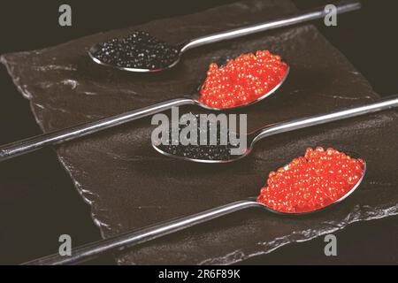 Deux cuillères en acier inoxydable remplies de caviar rouge et noir, placées côte à côte sur un fond blanc Banque D'Images