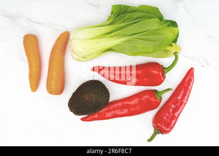 Un comptoir de cuisine bien éclairé présentant une variété de légumes vivants, y compris des carottes, des poivrons et des concombres, disposés de façon organisée Banque D'Images