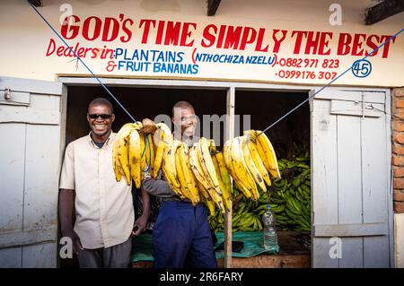 Deux hommes se tiennent à l'extérieur de leur boutique de bananes sur le marché de Mzuzu, au Malawi Banque D'Images