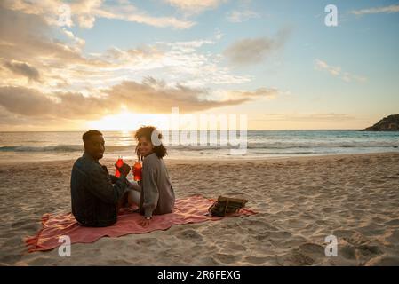 Un jeune couple multiethnique souriant profite d'un coucher de soleil sur la plage Banque D'Images