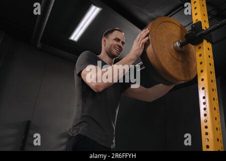 Joyeux athlète crossfit souriant mettant sur plus de poids sur barbell, en préappariement pour l'entraînement d'haltérophilie à la salle de gym. Musculate jeune homme s'exerçant avec une barbell lourde dans le cadre de l'entraînement fonctionnel Banque D'Images