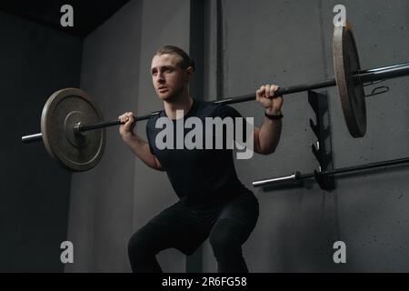 Athlète crossfit forte ayant l'entraînement et le culturisme avec des cloches de musculation squat dans le club de fitness. Un jeune homme de fitness musclé qui pèse un poids dans la salle de gym. Entraînement fonctionnel, haltérophilie Banque D'Images