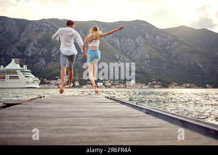 Couple en train de courir sur un quai en bois à la mer. Liberté, convivialité, concept de style de vie. Banque D'Images