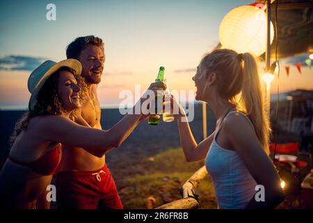 Un groupe d'amis toasts tout en buvant un beau coucher de soleil dans le camp pendant des vacances dans la nature. Vacances, amitié, camping, nature Banque D'Images
