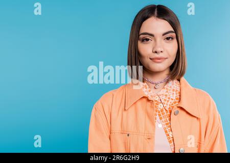 génération z, portrait de jolie femme, jeune mannequin de mode regardant l'appareil photo sur fond bleu, chemise orange, cheveux courts de brunette, nez percé, somme Banque D'Images