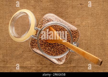 Céréales sèches et assaisonnements dans des tasses en bois avec des cuillères en bois sur une table en bois, macro, vue de dessus. Banque D'Images