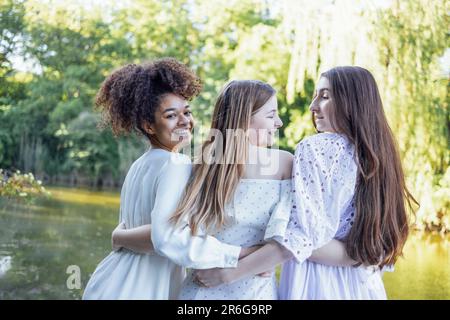 Trois jolies adolescentes multiraciales blanches dans des robes élégantes sont embrassant et riant. Souriante les filles drôles ont beaucoup de temps ensemble. Amitié Banque D'Images