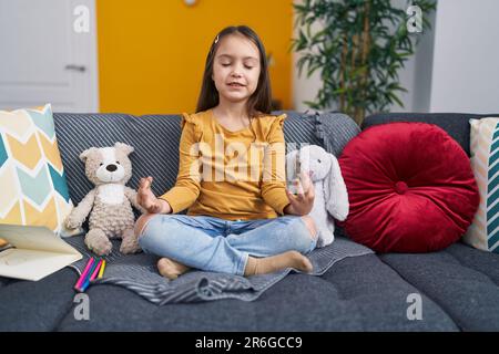 Adorable fille hispanique faisant de l'exercice de yoga assis sur le canapé à la maison Banque D'Images