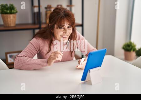 Femme d'âge moyen effectuant un test d'antigène covid-19 assis sur une table à la maison Banque D'Images