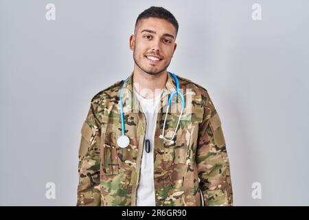 Jeune médecin hispanique portant un uniforme militaire de camouflage avec un sourire heureux et frais sur le visage. personne chanceux. Banque D'Images