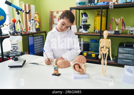 Adorable fille hispanique, étudiante scientifique, écrivant sur un carnet dans une salle de classe de laboratoire Banque D'Images