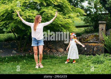 Jeune mère dansant avec petite fille mignonne dans le jardin, famille passant du temps ensemble Banque D'Images