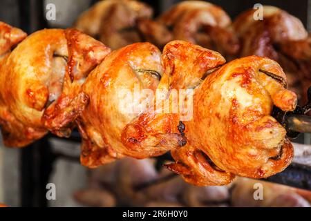 Gros plan de poulet entier rôti avec une savoureuse peau dorée sur une rôtisserie dans une rangée dans une cabine de cuisine de rue Banque D'Images