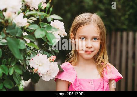 Portrait d'été extérieur de la petite fille adorable, beau enfant heureux dans le jardin avec des roses Banque D'Images