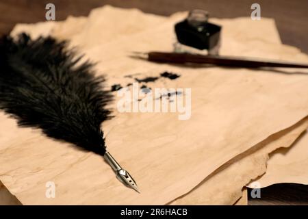 Différents stylos, encre et papier parchemin vintage avec taches d'encre sur la table, gros plan Banque D'Images