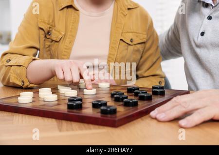 Jouer aux vérificateurs. Homme senior apprenant femme à table dans la chambre, gros plan Banque D'Images