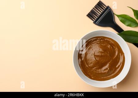 Bol de crème de henné, pinceau et feuilles vertes sur fond beige, plat avec espace pour le texte. Coloration naturelle des cheveux Banque D'Images