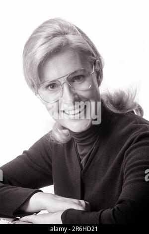 1970S PORTRAIT D'UNE FEMME BLONDE SOURIANTE PORTANT DES LUNETTES DE STYLE AVIATEUR REPOSANT SUR DES BRAS PLIÉS REGARDANT L'APPAREIL PHOTO - O4120 HAR001 HARS MAISON VIE COPIE ESPACE FEMMES PERSONNES CONFIANCE LUNETTES EXPRESSIONS B&W REPOS OEIL CONTACT VISION OPTIQUE JOLI BONHEUR TÊTE ET ÉPAULES SOURIRES GAIES AVIATEUR SYMPATHIQUE JOYFUL ÉLÉGANT JEUNE FEMME ADULTE NOIR ET BLANC CAUCASIEN ETHNICITÉ HAR001 VIEUX MODE Banque D'Images