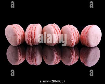 Une image de cinq macarons roses assortis disposés sur une surface réfléchissante Banque D'Images