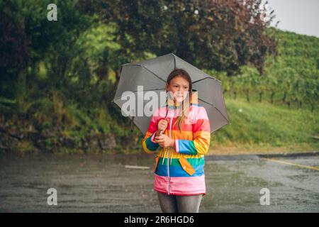 Portrait extérieur de la jeune fille sous la pluie, tenant un parapluie, portant une veste de pluie colorée Banque D'Images