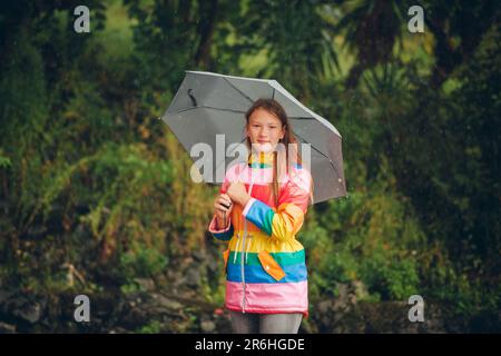 Portrait extérieur de la jeune fille sous la pluie, tenant un parapluie, portant une veste de pluie colorée Banque D'Images