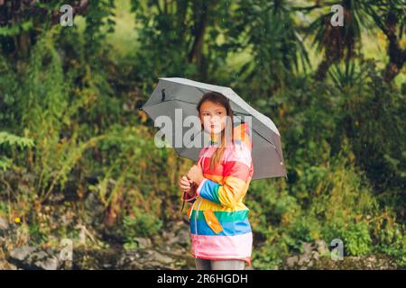 Portrait extérieur de la jeune fille sous la pluie, tenant un parapluie, portant une veste de pluie colorée Banque D'Images