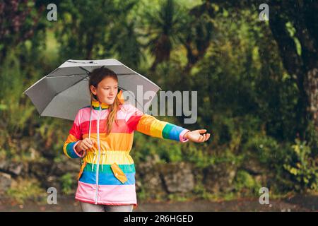 Portrait extérieur de la jeune fille sous la pluie, tenant un parapluie, portant une veste de pluie colorée Banque D'Images