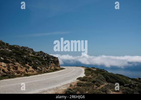 Une route solitaire sur une colline et des nuages au même niveau dans les cyclades d'iOS Grèce Banque D'Images