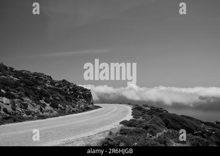 Une route solitaire sur une colline et des nuages sur le même niveau dans les cyclades iOS Grèce en noir et blanc Banque D'Images