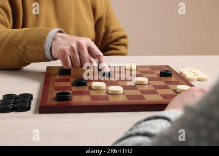 Homme senior jouant des dames avec partenaire à table en bois blanc, gros plan Banque D'Images