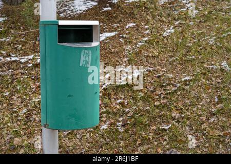 Poubelle verte sur poteau métallique avec herbe et neige en arrière-plan Banque D'Images