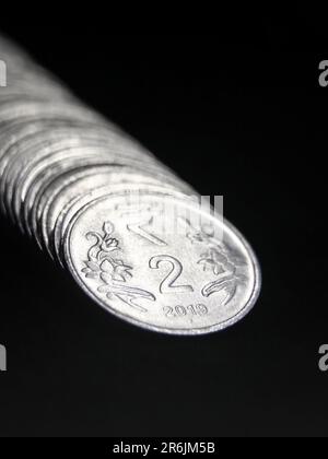 pièces d'argent brillantes de 2 ou deux roupies de l'inde disposées dans une rangée droite empilée isolée dans un fond noir dans macro de gros plan Banque D'Images