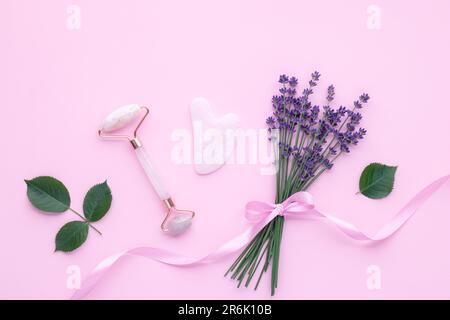 Rouleau frontal en quartz sur fond rose, vue de dessus. Outil de massage du visage. Soins de la peau, concept de traitement. Masseur Gua sha en jade et rose naturelles Banque D'Images