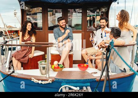 Un groupe d'amis se détend à l'arrière du bateau, en dégustant un apéritif avec des fruits frais et du champagne. Ils sourient et plaisantent ensemble car le bateau est d Banque D'Images