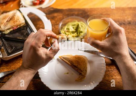 Un homme méconnaissable mange du pain grillé sur une assiette. Heure du petit déjeuner. Les mains de l'homme tiennent un couteau et une fourchette. Banque D'Images