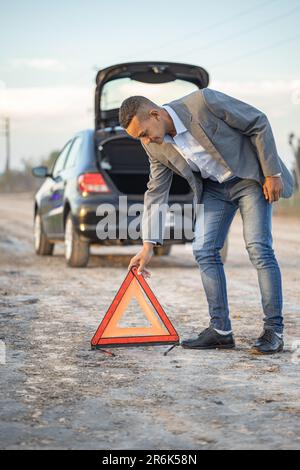 Jeune homme Latino plaçant un triangle d'avertissement derrière une voiture en panne. Banque D'Images