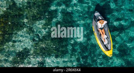 Une femme solitaire dans un chapeau de paille souriant, reposant couché flottant dans un kayak sur les vagues turquoises de la mer Adriatique. Vue aérienne du dessus de la côte. Exotique c Banque D'Images