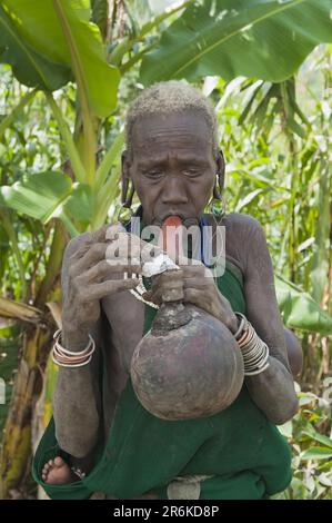 Vieille femme Surma fumant d'une pipe de gourde, Kibish, Omo Valley, Ethiopie Banque D'Images