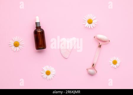 Rouleau à cadran en quartz et flacon en verre avec pipette sur fond rose, vue de dessus. Outil de massage du visage. Soins de la peau, concept de traitement. Masseur Gua sha fabriqué Banque D'Images