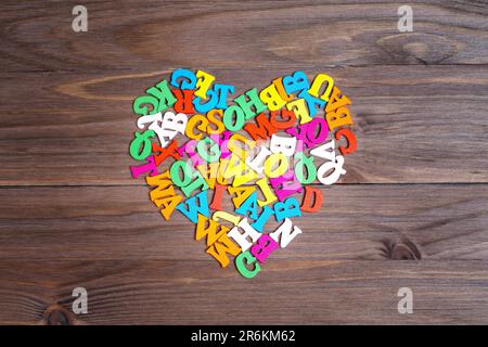 Lettres de l'alphabet en bois multicolore disposées en un symbole de coeur sur un fond en bois foncé. Concept de motivation d'apprentissage dynamique. Banque D'Images