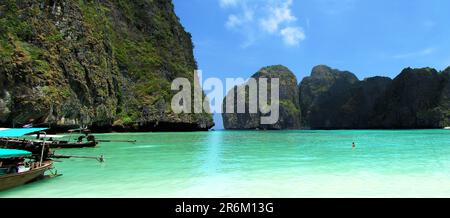 Une flotte de bateaux est amarrée dans une mer tranquille entourée de falaises vertigineuses, offrant une toile de fond pittoresque Banque D'Images