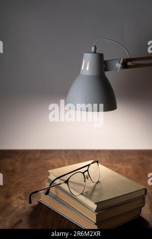 La lampe de bureau éclaire le lieu de travail sur la pile de livres et de lunettes du bureau Banque D'Images