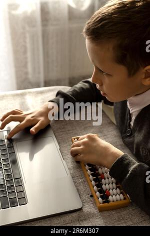 Un garçon de 10 ans apprend les mathématiques mentales avec un ordinateur portable et abacus Banque D'Images