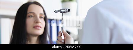 Le neurologue vérifie les réflexes à l'aide d'un marteau spécial tout en examinant une jeune patiente dans un cabinet médical Banque D'Images