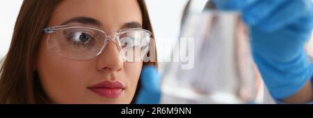 Portrait d'une femme scientifique dans des verres tient flacon avec liquide transparent Banque D'Images