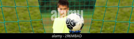 Bannière 1x4 avec un jeune gardien de football dans la porte en bokeh tient une balle attrapée Banque D'Images